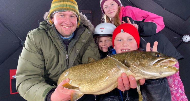 Jon Gorgas and his family hold up a large fish that they caught while ice fishing on a lake