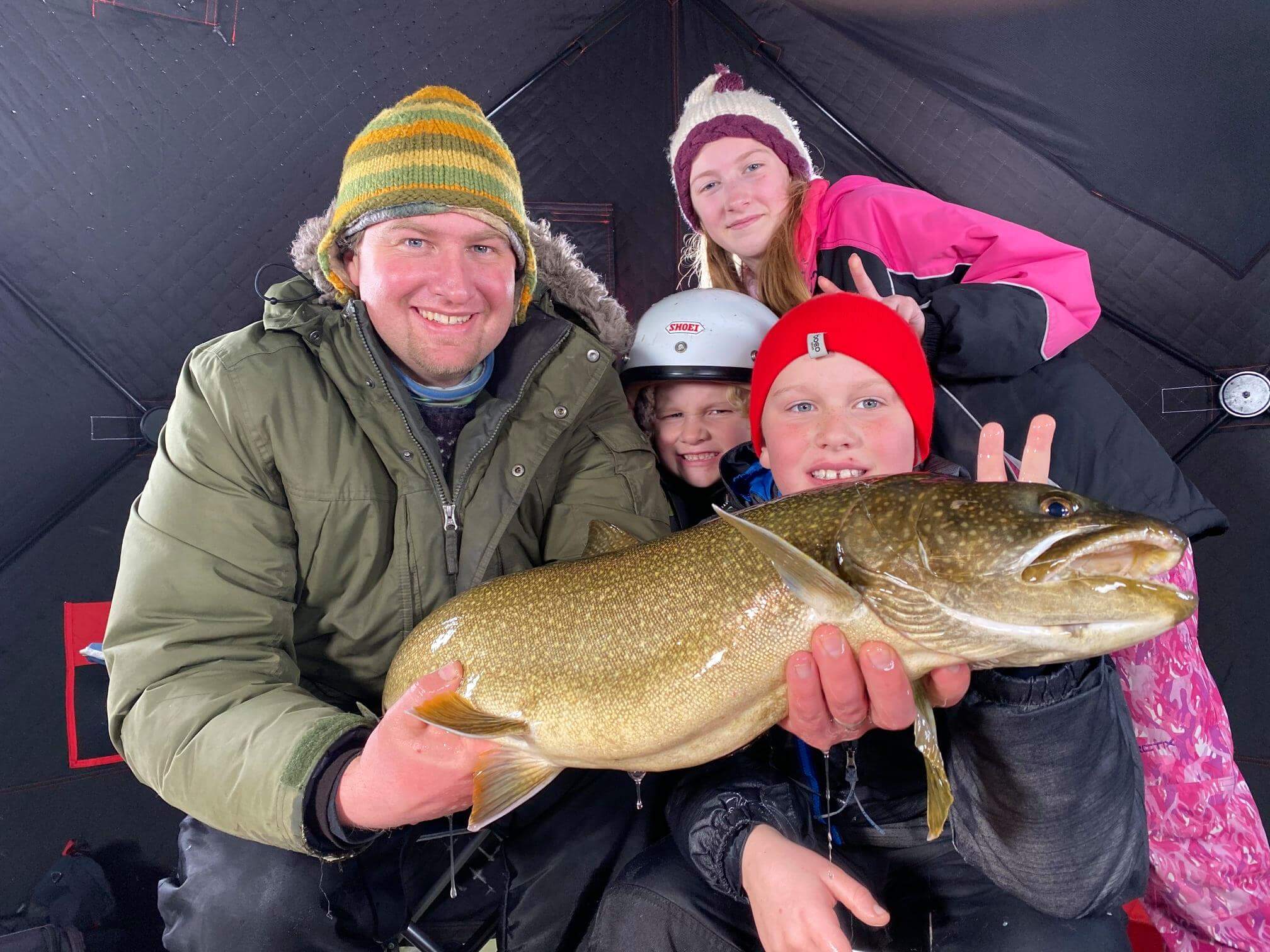 Jon Gorgas and his family hold up a large fish that they caught while ice fishing on a lake