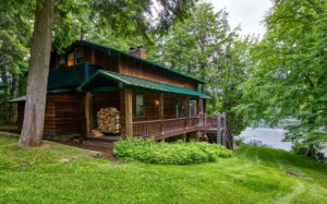 A lovely lakefront Adirondack cabin surrounded by lush green trees and a well manicured lawn