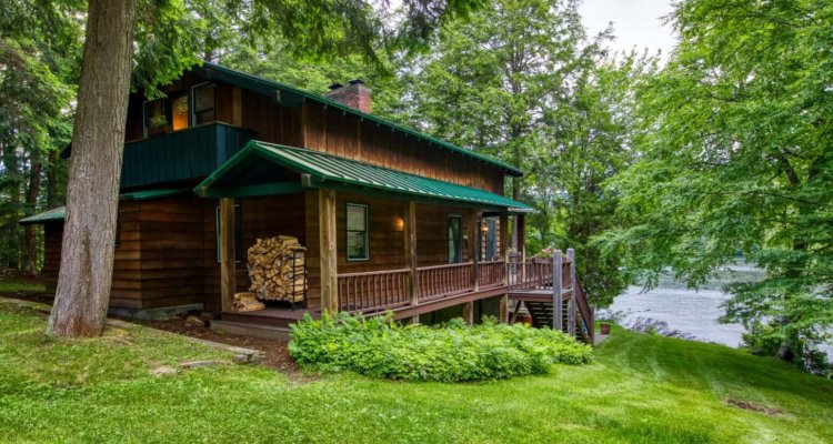 A lovely lakefront Adirondack cabin surrounded by lush green trees and a well manicured lawn