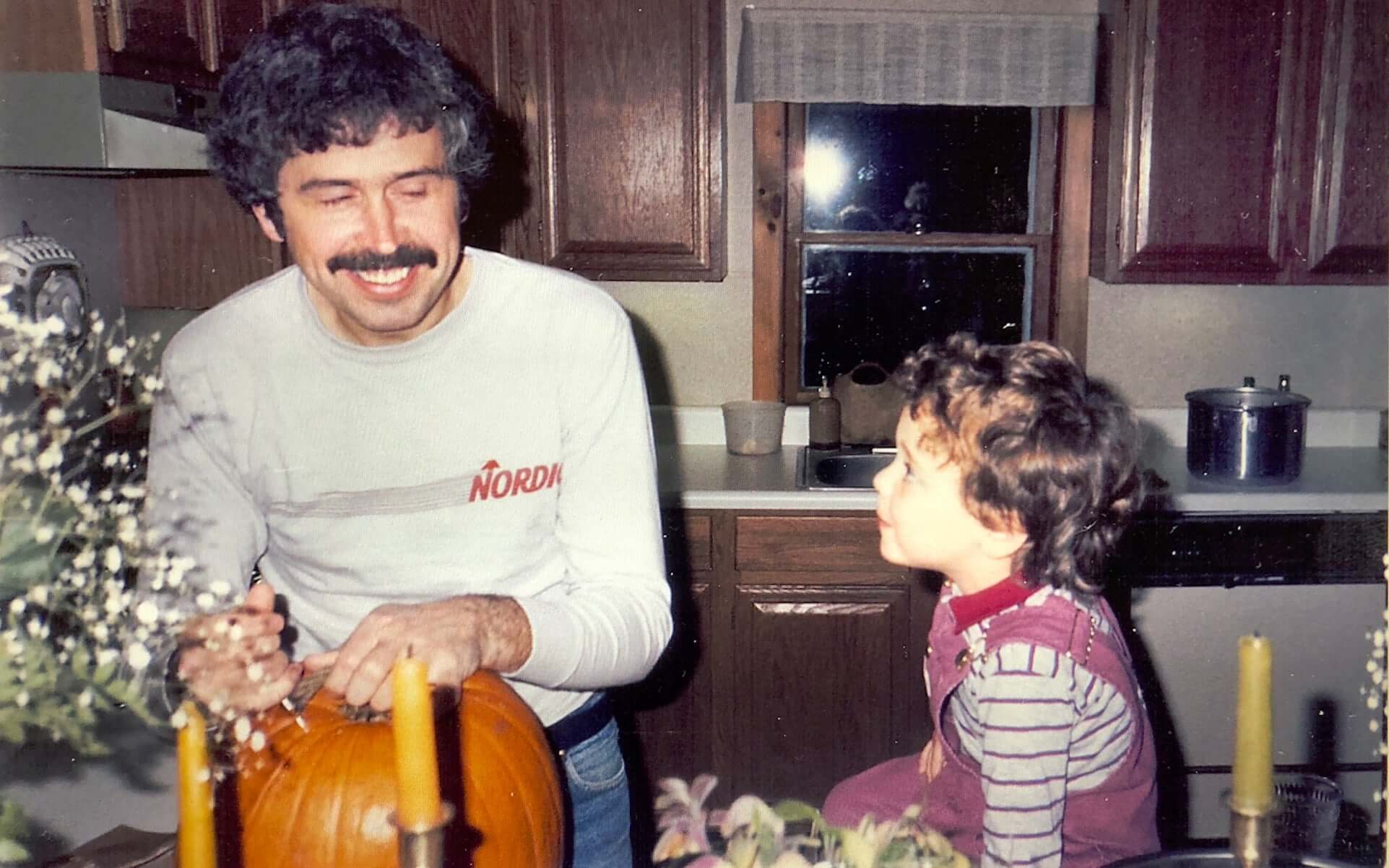 Old family photo showing Robert Politi smiling and carving a pumpkin while his son Nick watches on