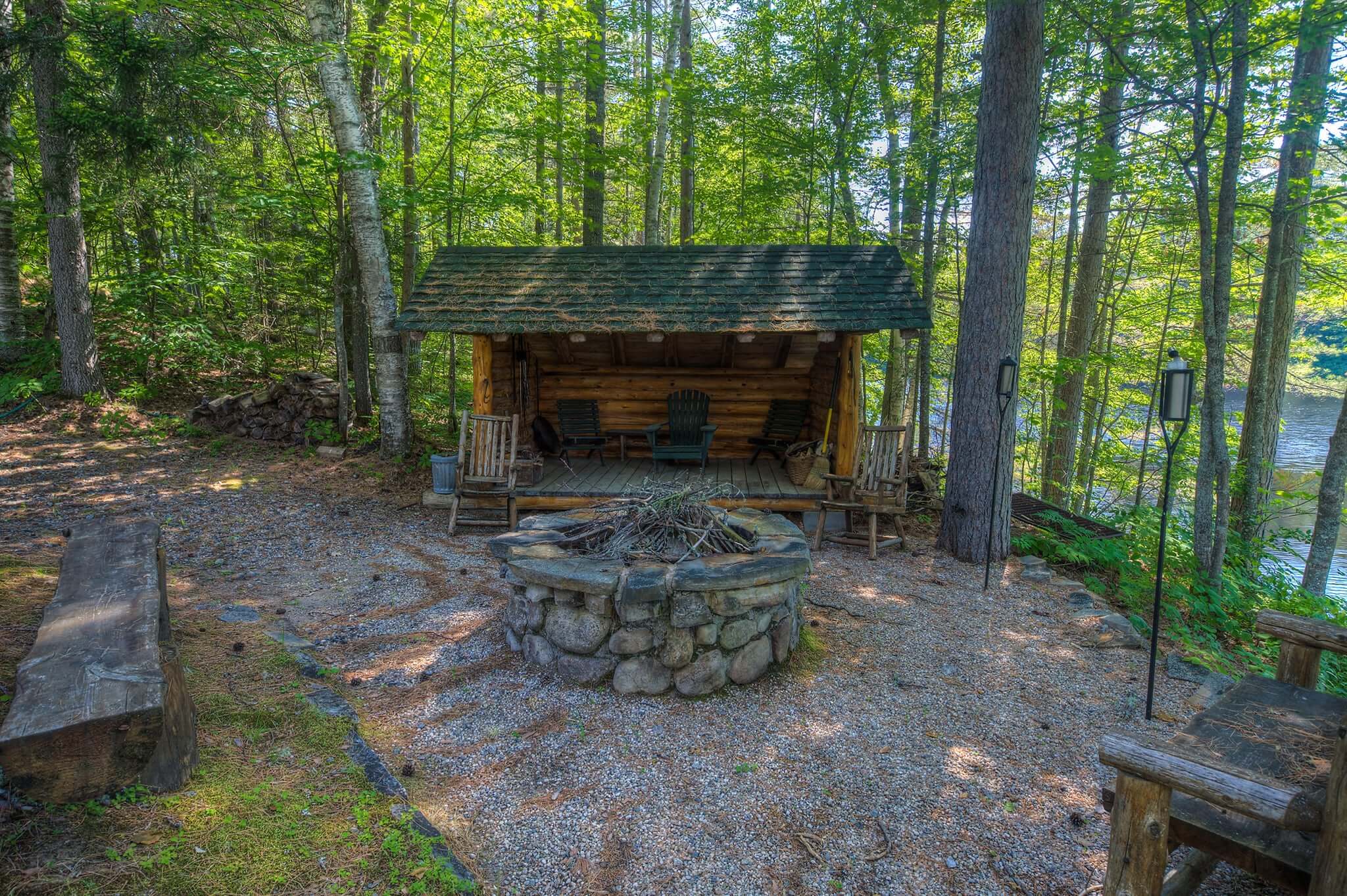 A log cabin-style lean-to sits behind a stone fire pit waiting for visitors to cozy up next to it