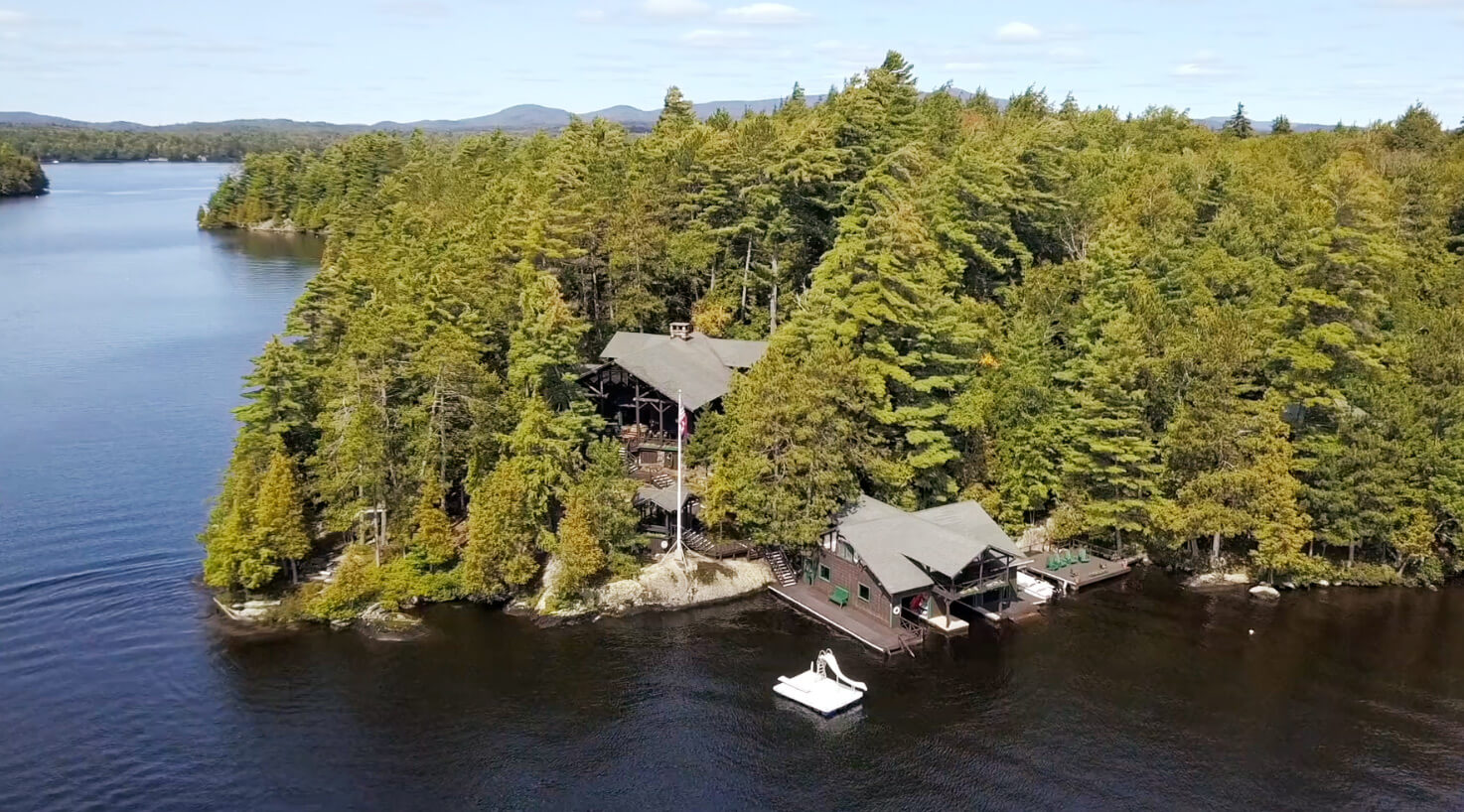 An aerial view of a beautiful estate nestled between trees and the shoreline of an Adirondack lake
