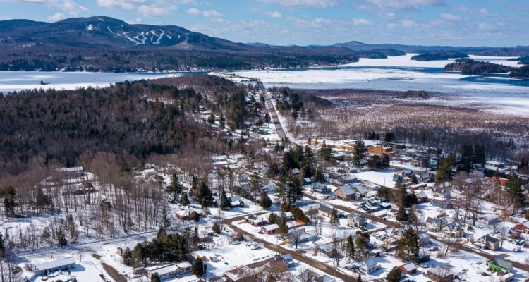 An aerial view of the village of Lake Placid during winter; landscape is flecked with snow and the lake is frozen